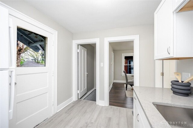 kitchen with light stone countertops, light wood-style floors, white cabinetry, and baseboards