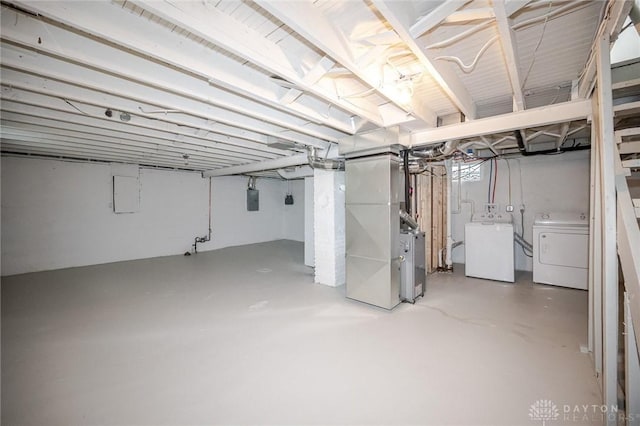 unfinished basement featuring electric panel, washing machine and dryer, and heating unit