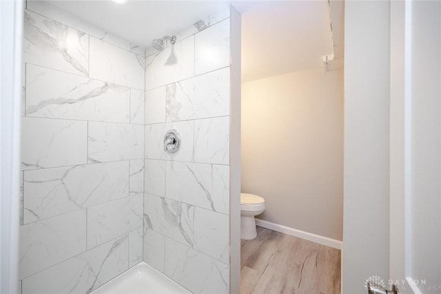 full bathroom with toilet, tiled shower, wood finished floors, and baseboards