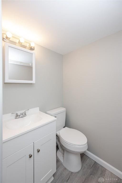 bathroom with toilet, vanity, wood finished floors, and baseboards
