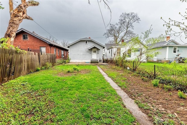 rear view of house with entry steps, driveway, fence private yard, and a lawn