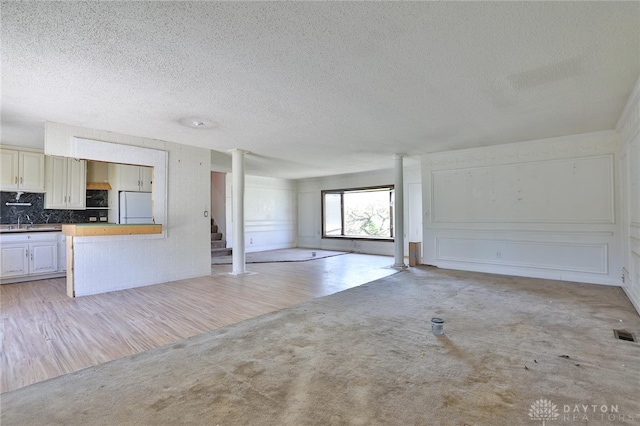 unfurnished living room featuring stairway, ornate columns, light carpet, a sink, and a textured ceiling