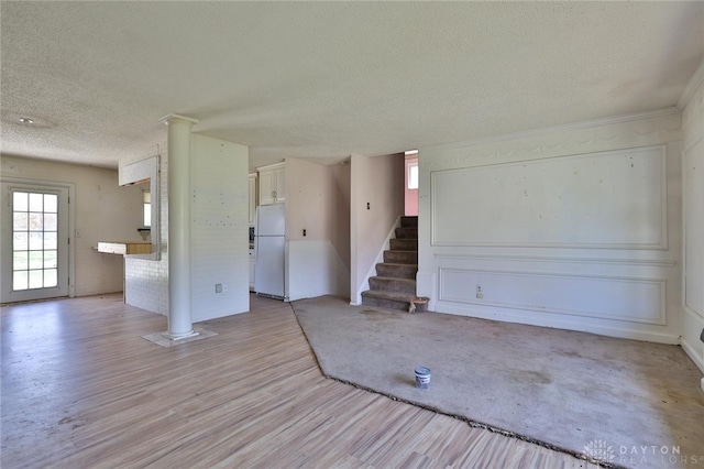 unfurnished living room featuring stairway, light wood-style floors, a textured ceiling, and plenty of natural light