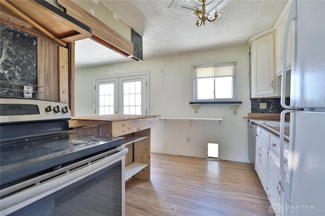 kitchen featuring white cabinets, a textured ceiling, light wood-type flooring, brick wall, and appliances with stainless steel finishes
