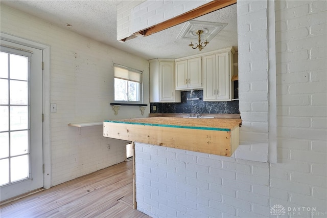 kitchen with a textured ceiling, a sink, decorative backsplash, light wood finished floors, and light countertops