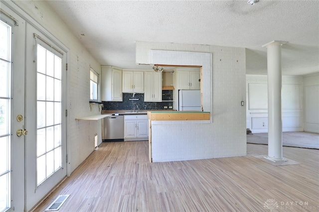 kitchen featuring a textured ceiling, dishwasher, freestanding refrigerator, light wood-style flooring, and ornate columns