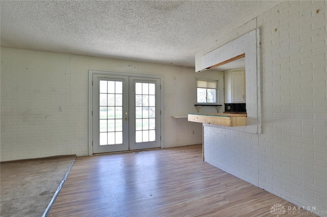 interior space with light wood finished floors, french doors, a textured ceiling, visible vents, and brick wall