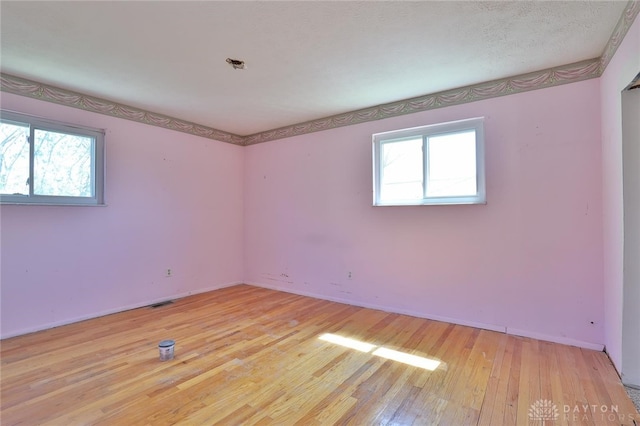 empty room featuring a healthy amount of sunlight, light wood finished floors, baseboards, and visible vents