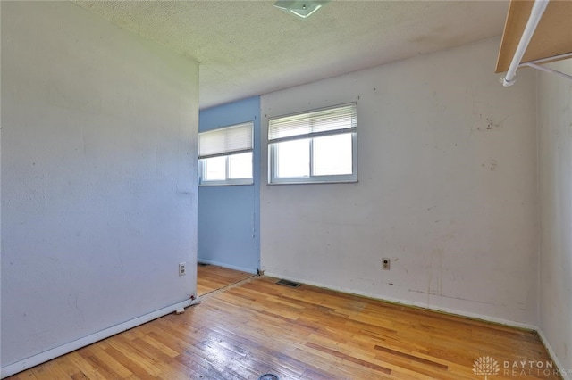 unfurnished room featuring hardwood / wood-style floors, baseboards, visible vents, and a textured ceiling