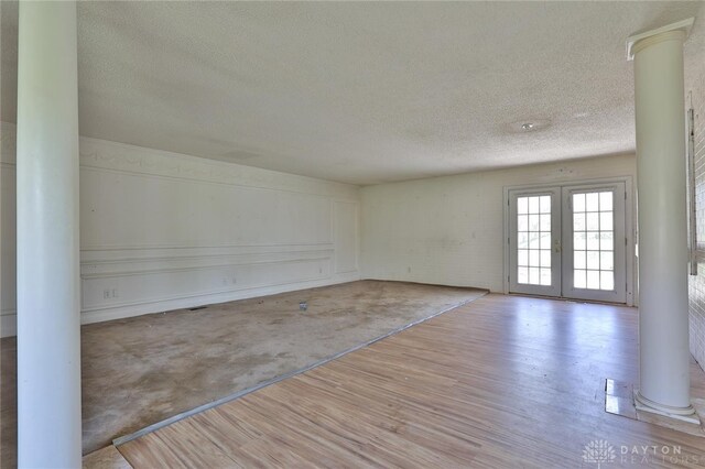 unfurnished room with wood finished floors, french doors, a textured ceiling, and ornate columns