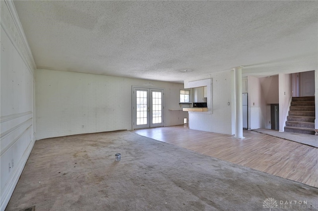 unfurnished living room featuring light carpet, french doors, a textured ceiling, and stairs