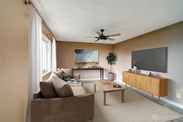 living room with a textured ceiling, wood finished floors, ceiling fan, and baseboards