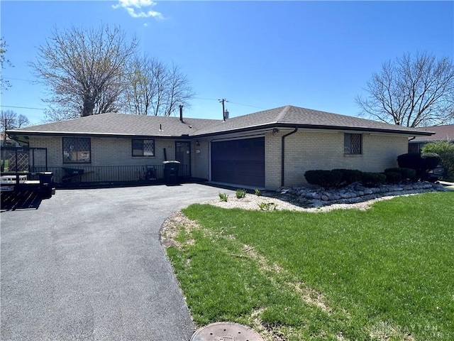 single story home featuring a front yard, a garage, aphalt driveway, brick siding, and roof with shingles