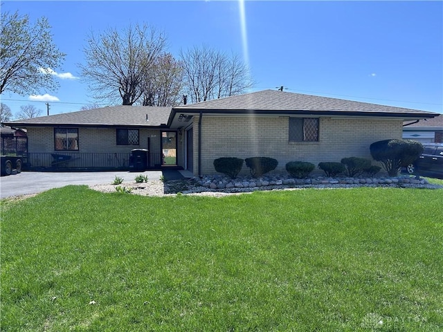 ranch-style home with a front yard, brick siding, driveway, and roof with shingles