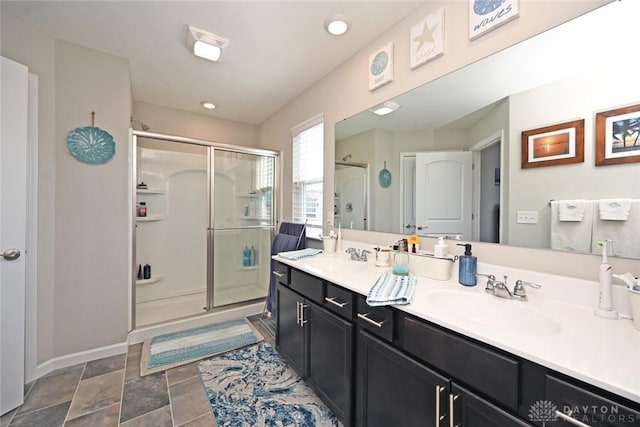 full bath with a sink, baseboards, a shower stall, and double vanity