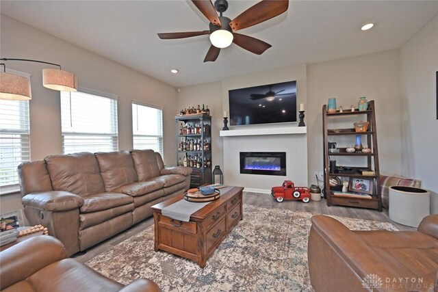 living area featuring recessed lighting, a ceiling fan, a glass covered fireplace, and wood finished floors