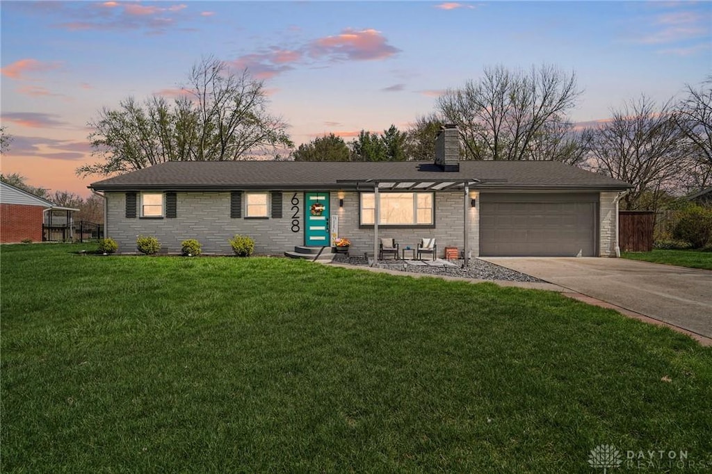 single story home with a chimney, a garage, driveway, stone siding, and a front yard