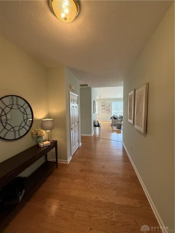 corridor featuring baseboards, wood finished floors, and a textured ceiling
