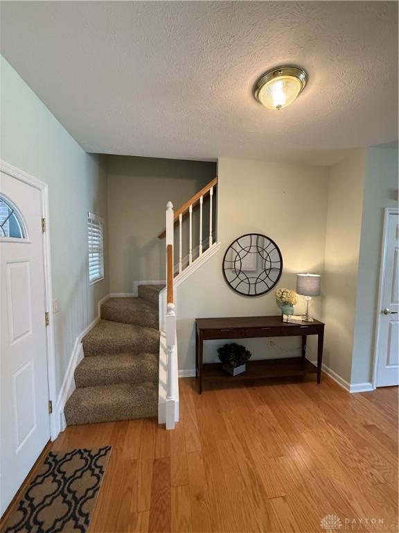entrance foyer with baseboards, a textured ceiling, wood finished floors, and stairs