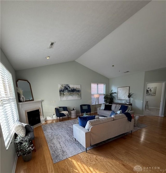 living room featuring plenty of natural light, lofted ceiling, wood finished floors, and a fireplace with flush hearth