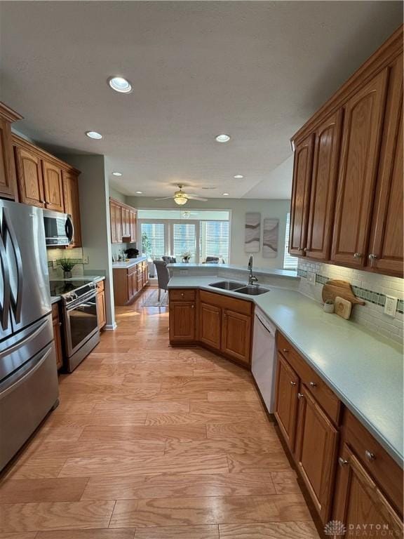 kitchen with brown cabinetry, a peninsula, appliances with stainless steel finishes, and a sink