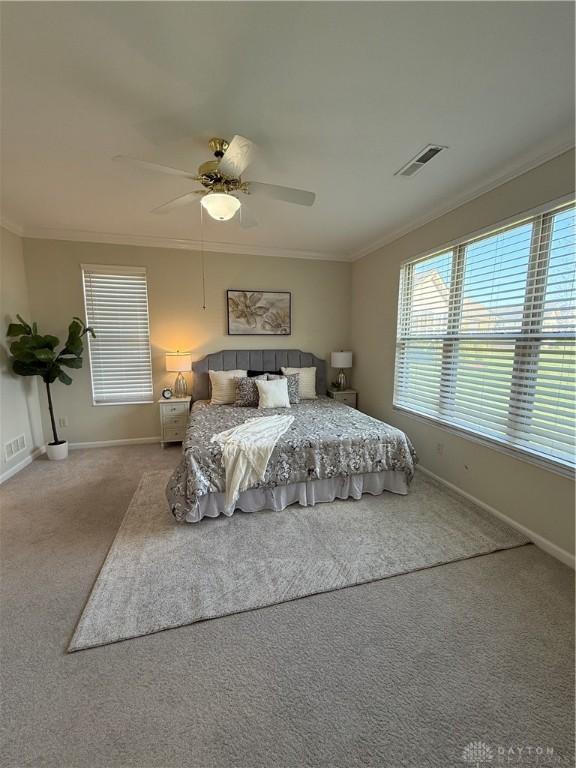 carpeted bedroom with visible vents, baseboards, ornamental molding, and ceiling fan
