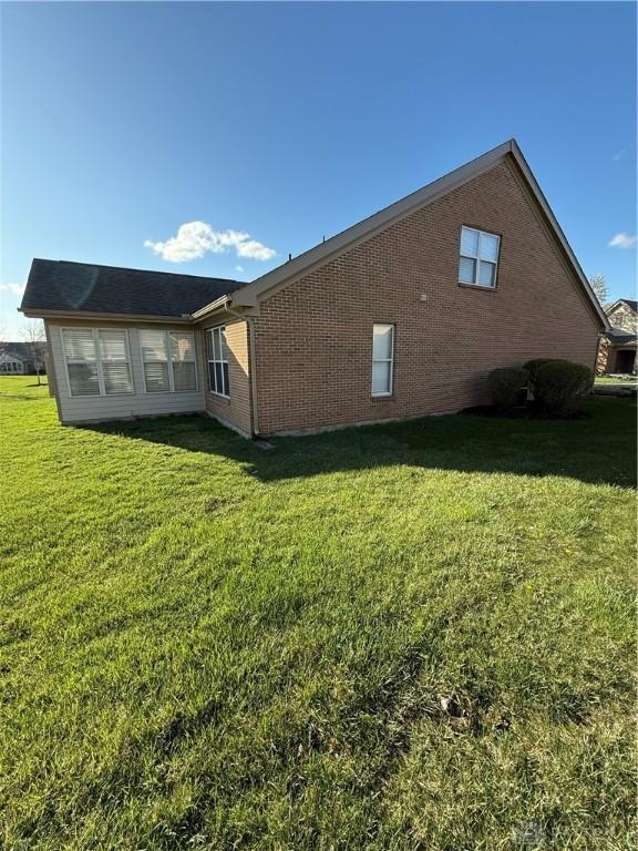 rear view of house featuring a yard and brick siding