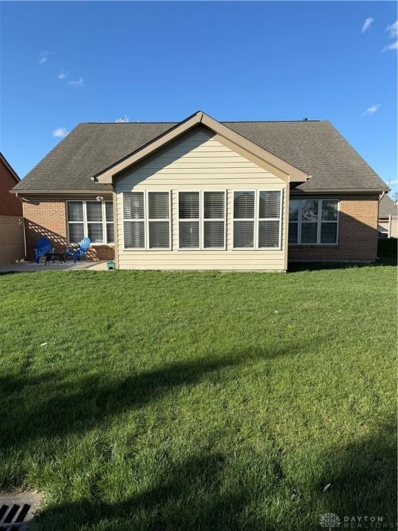 rear view of property with a lawn and roof with shingles