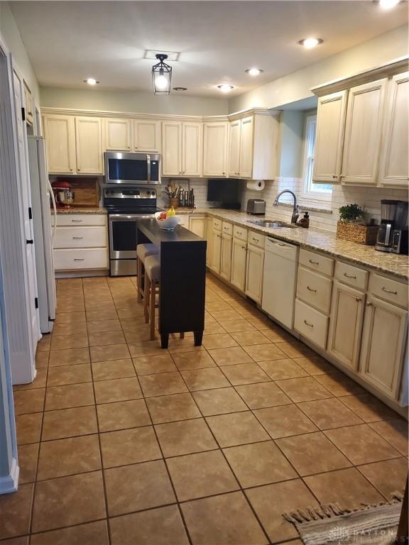 kitchen with appliances with stainless steel finishes, decorative backsplash, light tile patterned floors, and a sink