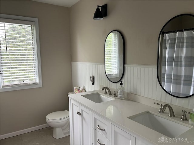 full bathroom with toilet, wainscoting, double vanity, and a sink