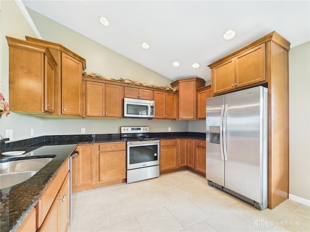 kitchen featuring dark stone counters, vaulted ceiling, a sink, stainless steel appliances, and brown cabinets