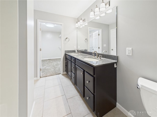 bathroom featuring toilet, double vanity, a sink, and baseboards