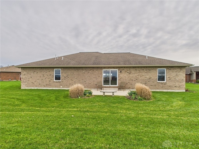 rear view of house featuring a patio area, brick siding, a lawn, and roof with shingles