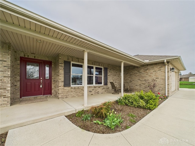 property entrance with a porch, an attached garage, and brick siding