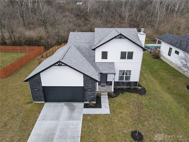 modern farmhouse featuring roof with shingles, fence, a front lawn, an attached garage, and concrete driveway