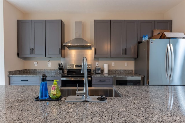kitchen with wall chimney exhaust hood, a sink, stainless steel appliances, decorative backsplash, and light stone counters