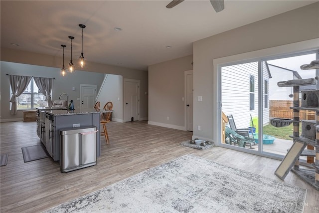 kitchen featuring pendant lighting, light wood-style floors, light stone countertops, a ceiling fan, and baseboards