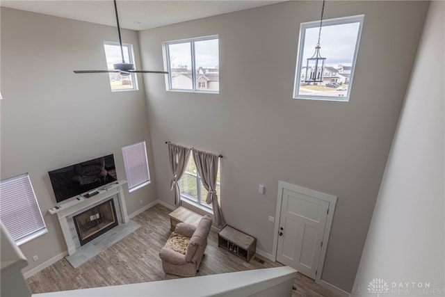living room with a premium fireplace, wood finished floors, a towering ceiling, and a ceiling fan