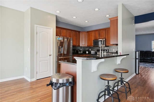 kitchen featuring a kitchen breakfast bar, a peninsula, light wood-type flooring, appliances with stainless steel finishes, and decorative backsplash