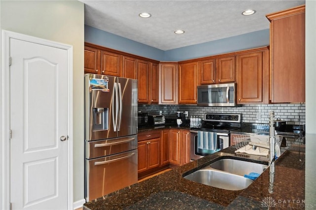 kitchen with brown cabinetry, dark stone countertops, decorative backsplash, and stainless steel appliances