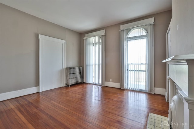 unfurnished living room featuring radiator heating unit, baseboards, a glass covered fireplace, and hardwood / wood-style flooring