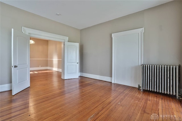 spare room featuring hardwood / wood-style floors, radiator heating unit, baseboards, and an inviting chandelier