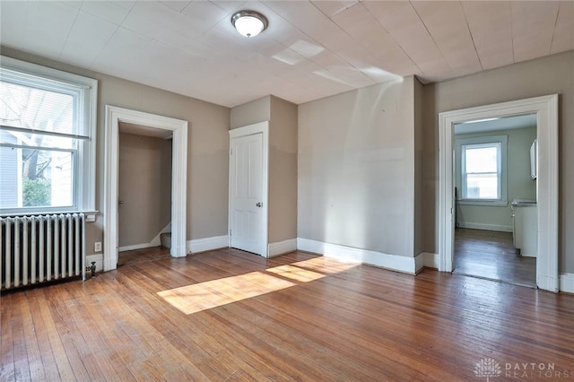 unfurnished room featuring radiator, hardwood / wood-style floors, and a healthy amount of sunlight