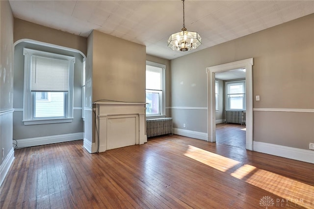 unfurnished room with wood-type flooring, a notable chandelier, baseboards, and radiator