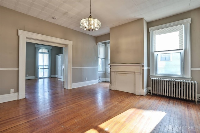 spare room featuring radiator heating unit, hardwood / wood-style floors, a notable chandelier, and a healthy amount of sunlight