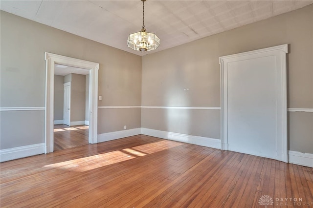 spare room with baseboards, hardwood / wood-style floors, and an inviting chandelier