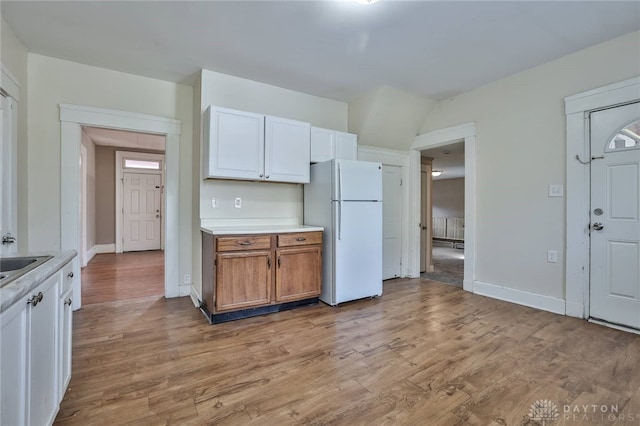 kitchen featuring baseboards, a sink, light countertops, freestanding refrigerator, and light wood-style flooring