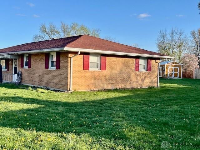 view of side of property with brick siding, a yard, a shed, and an outbuilding