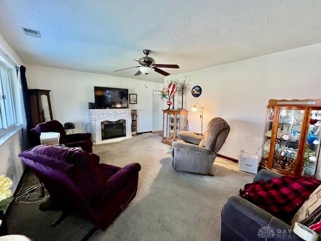 carpeted living area featuring visible vents, ceiling fan, a fireplace, and a textured ceiling