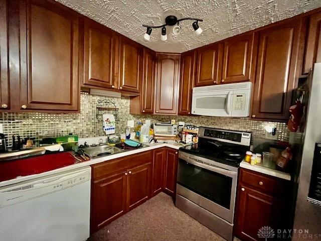 kitchen featuring appliances with stainless steel finishes, a textured ceiling, light countertops, decorative backsplash, and a sink